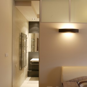 Cen­tral­nym punk­tem oszczę­d­nie urzą­dzo­nej sy­pial­ni jest du­że łóż­ko z sze­ro­kim za­głów­kiem (Bo Con­cept). Sztucz­ne oświe­tle­nie za­pew­nia­ją noc­ne lamp­ki z po­ma­rań­czo­wy­mi aba­żu­ra­mi i cze­ko­la­do­we kin­kie­ty umiesz­czo­ne na ścia­nie. Fot. Tomek Markowski.