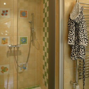 Wnętrze, umieszczonej we wnęce, kabiny prysznicowej powtarza kolorystykę zastosowaną w całej łazience. Frontową ściankę zdobią dwa rzędy wesołych dekorów. Fot. Monika Filipiuk.