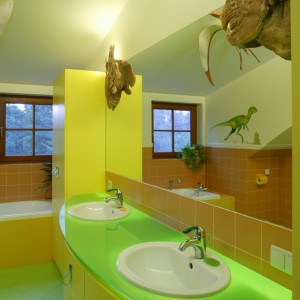 Głównym oświetleniem łazienki jest szklany blat umywalkowy, spod którego przenika mocne światło. Jego zieleń, podobnie jak posadzki, jest elementem stylizacji nawiązującym do pradawnej przyrody. Fot. Bartosz Jarosz.