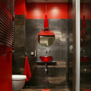 Gościnna toaleta to kwintesencja stylu mieszkania, a zarazem designerski smaczek. Ciemna tonacja wnętrza została ożywiona dokładnie zaplanowanymi detalami w energetycznym kolorze. Mozaikowy czerwony pas biegnący przez podłogę został przeniesiony na sufit. Fot. Monika Filipiuk.