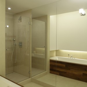 Kabina prysznicowa w łazience znalazła się pomiędzy wanną a ogromnym lustrem, pokrywającym jedną ze ścian. Lustro wywołuje optyczne złudzenie przestrzeni, co doskonale sprawdza się w wąskim i długim wnętrzu. 