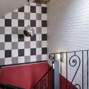 Do stylu glamour nawiązuje ozdobna poręcz przy schodach. Śmiałe połączenie szarości szachownicy i czerwonej, wzorzystej tapety na ścianach klatki schodowej dało zaskakujący efekt. Fot. Monika Filipiuk.