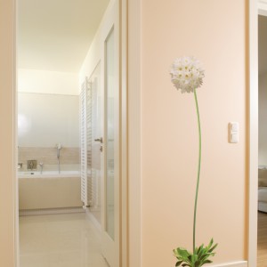 Obok sypialni małżeńskiej umiejscowiono łazienkę, do której można dostać się przez korytarz główny. Ogromny kwiat na przestrzeni między oboma pomieszczeniami przełamuje panującą w domu powściągliwość i surowość formy, dodając mu szczyptę subtelnego, kobiecego charakteru. Fot. Bartosz Jarosz.