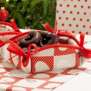 Kwadratowy koszyk na pieczywo, z kokardkami, wykończony lamówką, której kolor może być dobrany w zależności od tkaniny. Kolekcja tkanin Christmas. 31,90 zł, Dekoria. Fot. Dekoria.