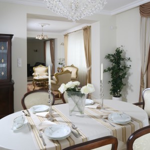 Biały obrus to klasyka eleganckiego nakrycia stołu. Tutaj dodatkowo skomponowano go z bieżnikami w złote pasy. Projekt wnętrza: Małgorzata Goś. Fot. Bartosz Jarosz. 