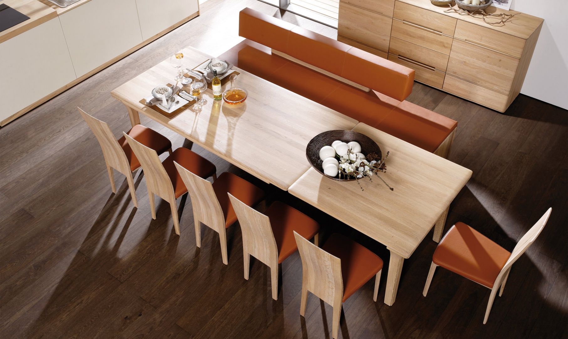 Pomarańczowa tapicerka krzeseł i nowoczesnej ławy sprawia, że jadalnia staje się jeszcze cieplejsza i zyskuje apetyczny wygląd. Fot. Voglauer.