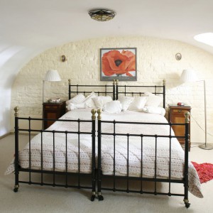 Kute łóżko doskonale prezentuje się na tle jasnej, ceglanej ściany. Klasyczne stoliki nocne, komoda oraz oświetlenie dodają wnętrzu uroku. Fot. Archiwum Dobrze Mieszkaj.