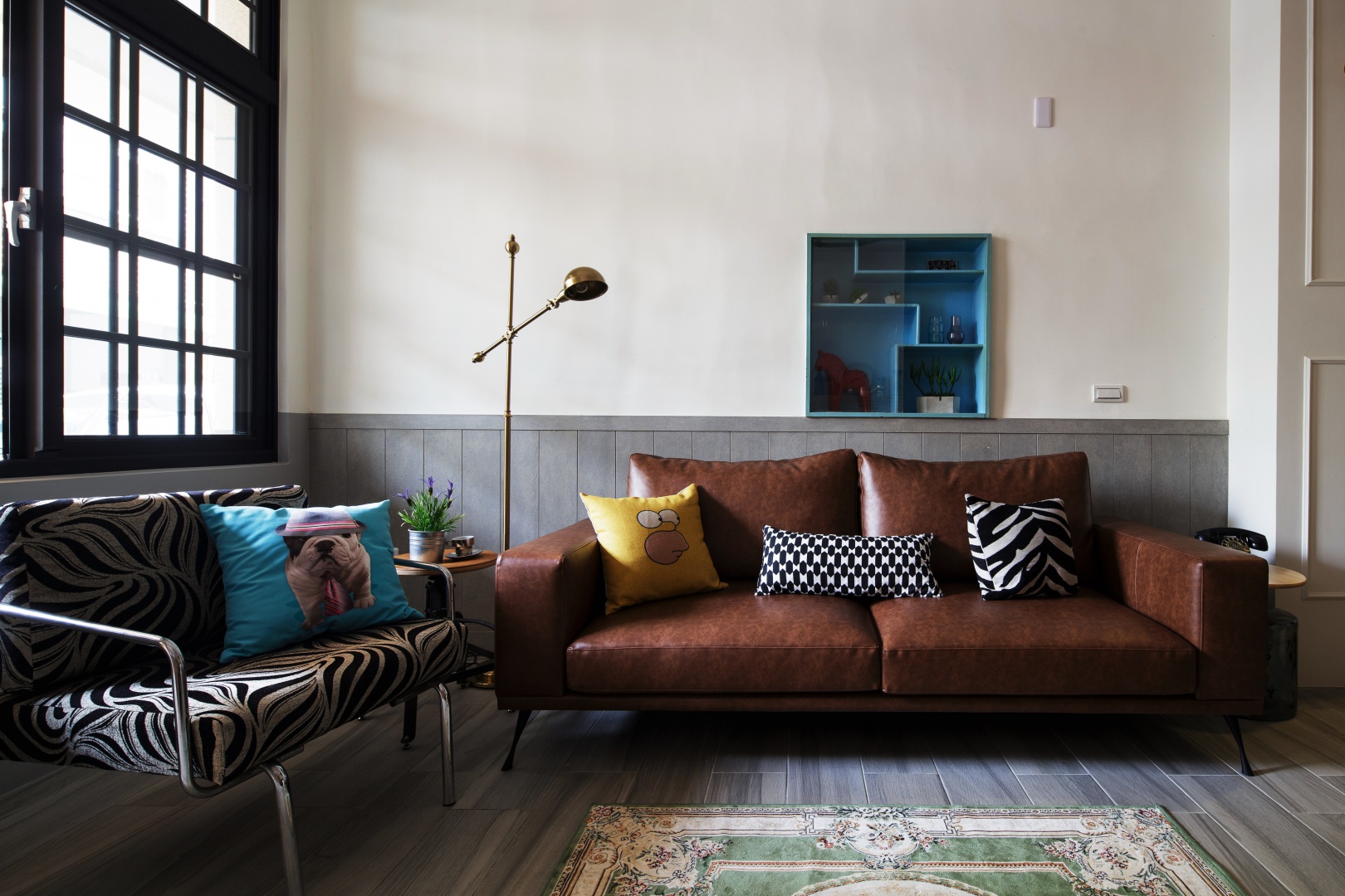 Tapicerowana, skórzana kanapa pięknie harmonizuje z drewnem na podłodze i ścianie. Naturalną kolorystykę przełamano ciemnym błękitem w postaci poduszki dekoracyjnej i niewielkiej, asymetrycznej szafki wiszącej na ścianie. Projekt: HAO Design Studio. Fot. Joey Liu.
