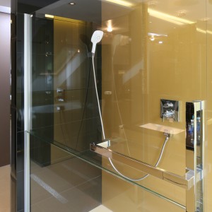 Ściana za prysznicem została zabezpieczona szkłem lakierowanym od spodu na złoty kolor, który świetnie współgra z innymi materiałami i kolorami składającymi się na aranżację tego luksusowego wnętrza. Projekt: Chantal Springer. Fot. Bartosz Jarosz.