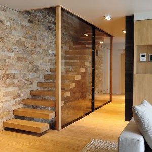 Schody wspornikowe z drewnianymi stopniami, idealnie wpasowują się w styl całego wnętrza. Wrażenie lewitowania pojedynczych stopni wzmaga szklana ścianka, zamykająca klatkę schodową. Projekt: Coblonal Arquitectura. Fot. Coblonal Arquitectura.