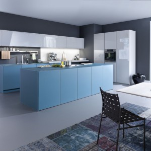 Oryginalna niebieska wyspa kuchenna utrzymana w nowoczesnej stylistyce. Kolor przepięknie komponuje się z połyskującymi szafkami górnymi i wysoką zabudową w bieli. Fot. Leicht, kolekcja Largo-FG. 