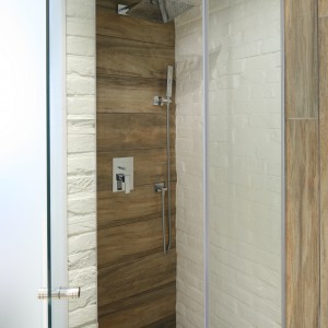 Kabinę prysznicową tworzą wąska ścianka boczna oraz otwierane wahadłowo drzwi. Zamiast brodzika – odpływ liniowy w posadzce. Fot. Bartosz Jarosz.