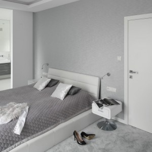 Sypialnia, podobnie jak pozostałe pomieszczenia w domu jest elegancka i urządzona minimalistycznie. Dominują tutaj modne szarości. Za przesuwnymi szklanymi drzwiami znajduje się łazienki pani i pana domu. Projekt: Katarzyna Mikulska-Sękalska. Fot. Bartosz Jarosz. 