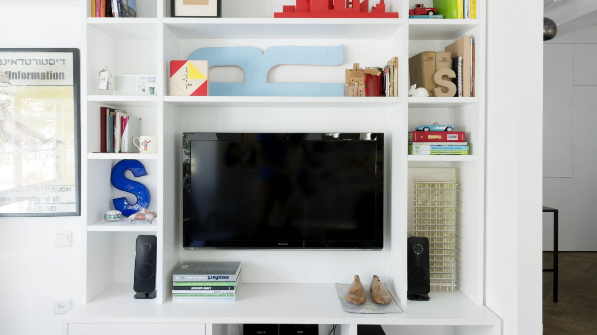 Telewizor w salonie wpasowano we wnękę, otoczoną licznymi, praktycznymi półkami. Mogą one posłużyć za miejsce wyeksponowania dekoracji lub wykorzystane jako biblioteczka. Projekt: Studio Raanan Stern. Fot. Gidon Levin.