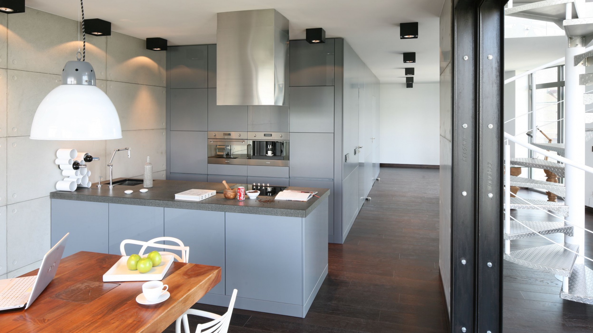 Kuchnia w stylu loft w przeważającej mierze jest szara. Szare, delikatnie wpadające w błękit są meble kuchenne oraz ściana wykończona betonem architektonicznym. Projekt: Justyna Smolec. Fot. Bartosz Jarosz.