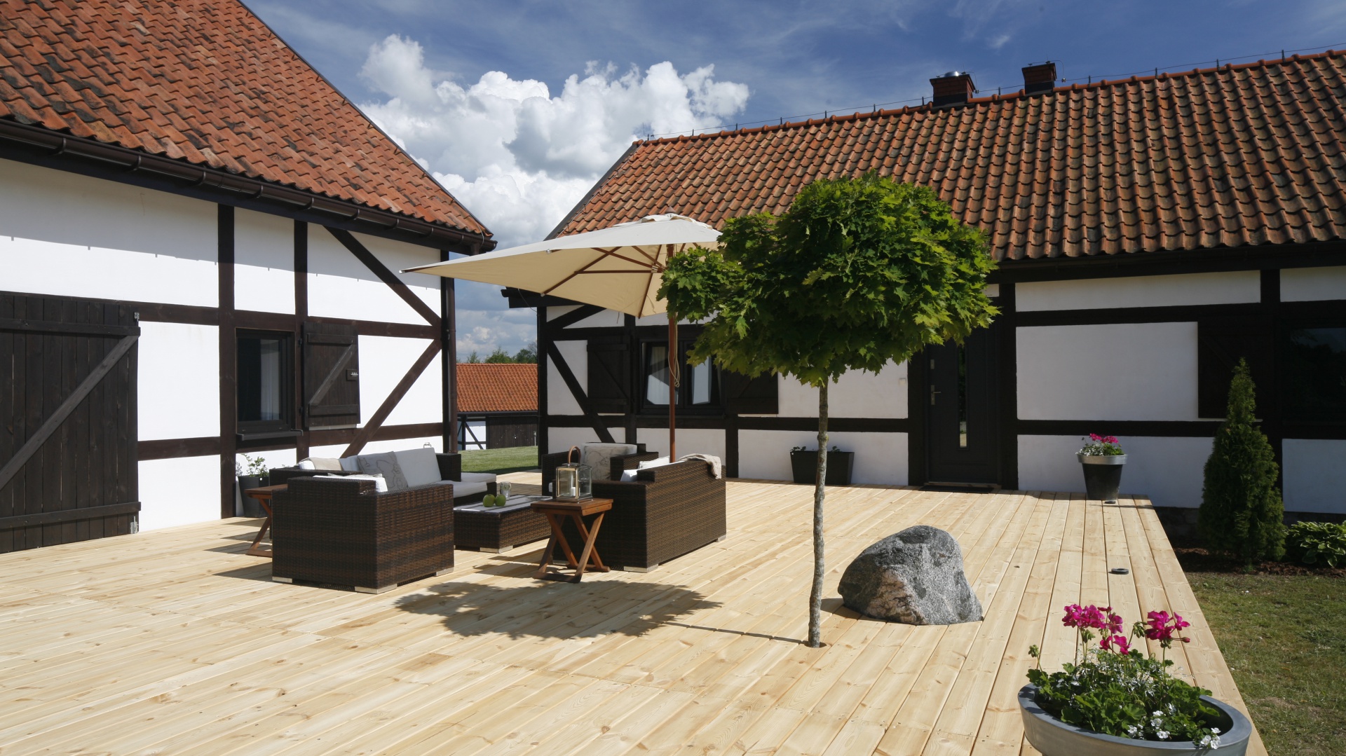Do architektury muru pruskiego idealnie pasuje prosty drewniany podest z uroczym drzewkiem. Więcej zieleni wprowadzają również eleganckie donice. Domownicy i goście mogą spocząć na eleganckich meblach, harmonizujących kolorem ze stolarką domu. Projekt: Kamila Paszkiewicz. Fot. Bartosz Jarosz