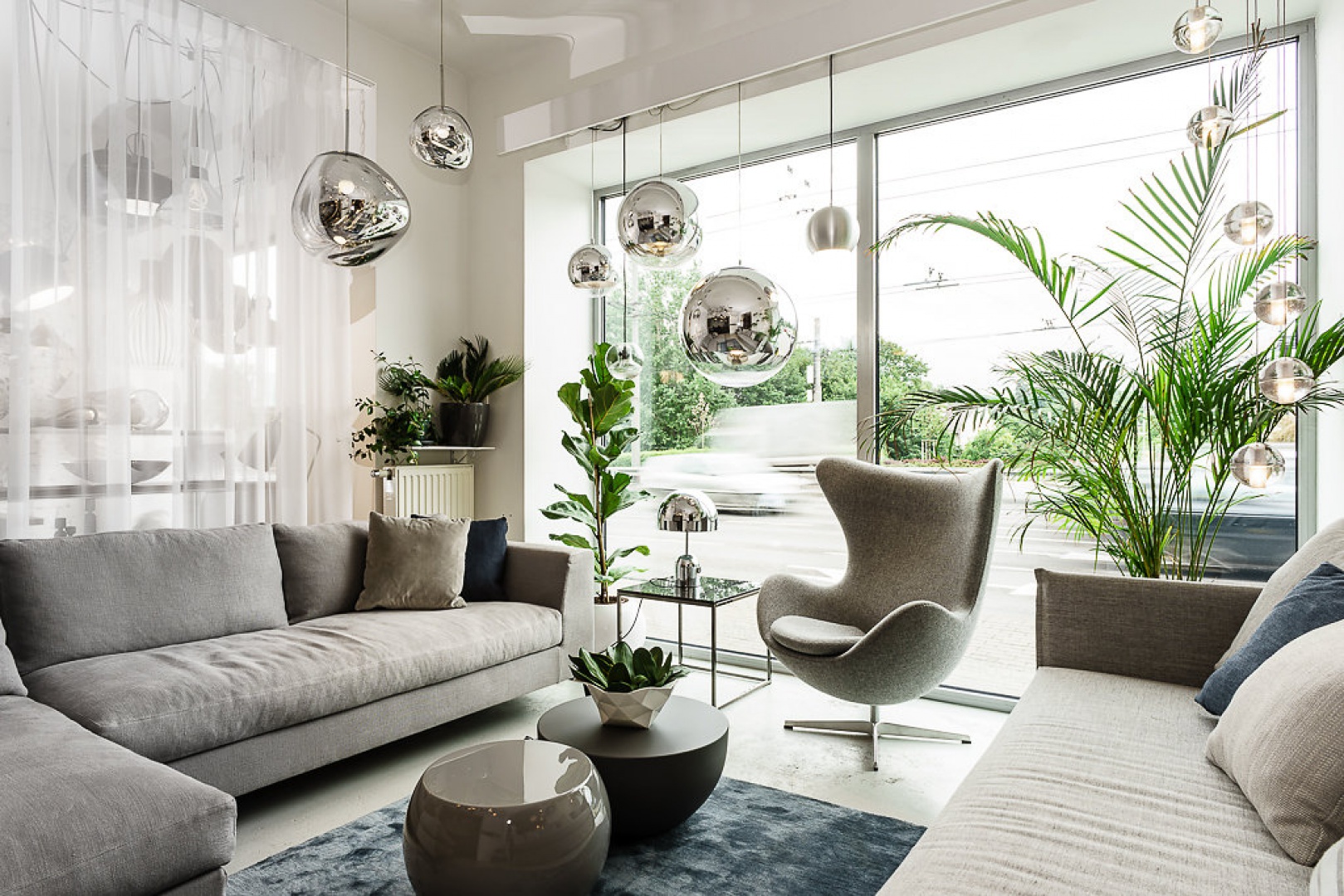 Liczne podwieszane srebrzyste kule i formy kulo-podobne stanowią oświetlenie w tym eleganckim szarym salonie. Fot. Mesmetric Concept Store