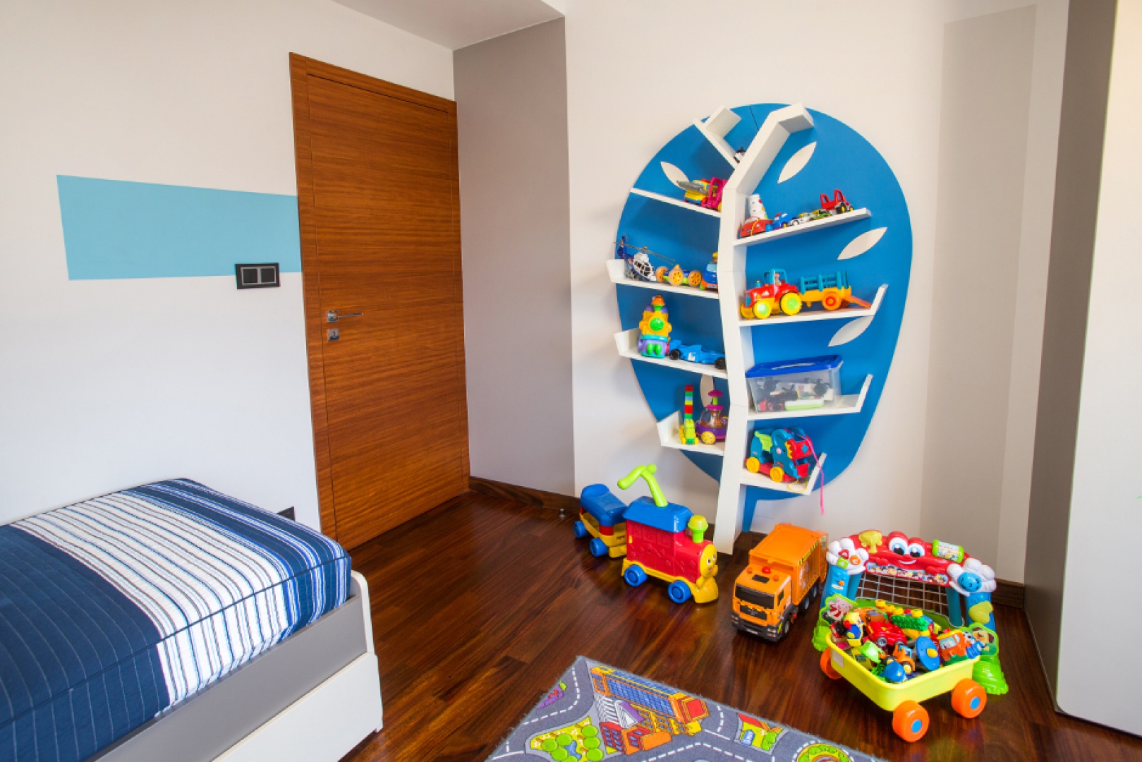 W pokoju synka na jednej ze ścian ustawiono fantazyjny mebel, z półkami imitującymi gałęzie drzew i gotowymi niebieskimi plecami w roli korony liści. Projekt: Pracownia Projektowania Wnętrz Viva Design, Fot. Tadeusz Poźniak.