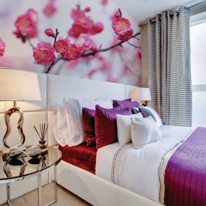 Ścianę nad łóżkiem zdobi kolorowa fototapeta ze zdjęciem pięknych kwiatów wiśni. Fot. Dekornik