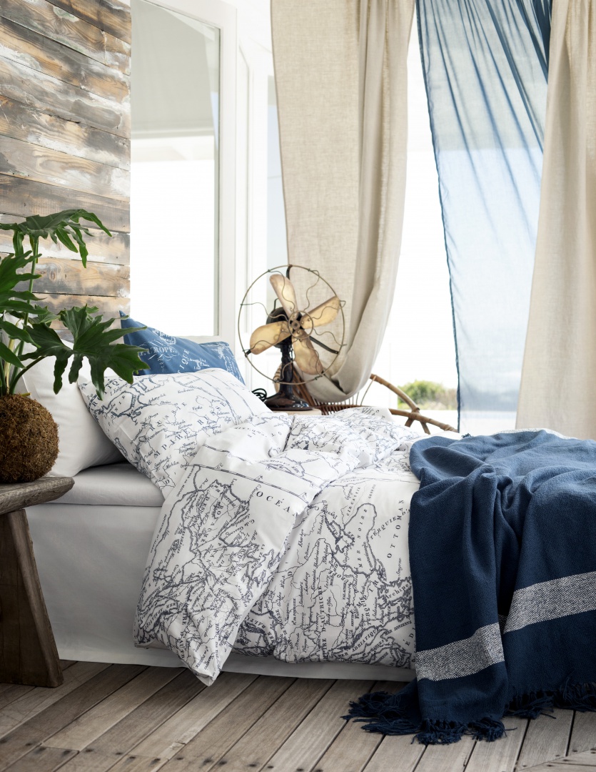 Przetarte drewno na podłodze i ścianie, do tego granatowo-biała pościel z kartograficznymi nadrukami. W tej sypialni króluje styl marynistyczny. Fot. H&M Home