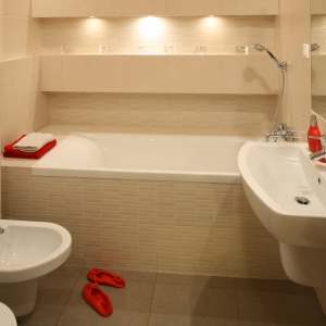 Ponadczasowe beże w łazience dla rodziny efektownie ożywiają czerwone dodatki. Projekt: właściciele. Fot. Bartosz Jarosz