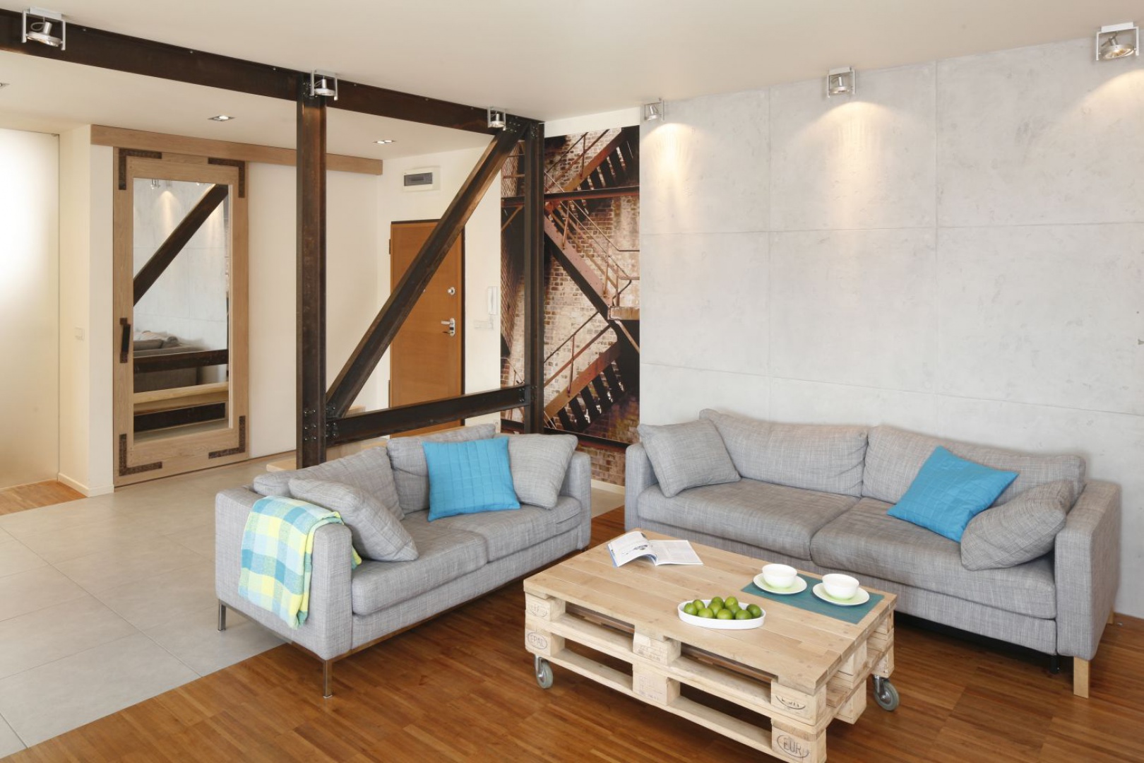 Salon w stylu loft swój charakter zyskał dzięki metalowym belkom, betonowi na ścianie oraz