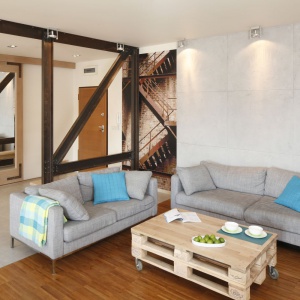Salon w stylu loft swój charakter zyskał dzięki metalowym belkom, betonowi na ścianie oraz "fabrycznej" fototapecie w holu. Projekt: Marta Kruk. Fot. Bartosz Jarosz