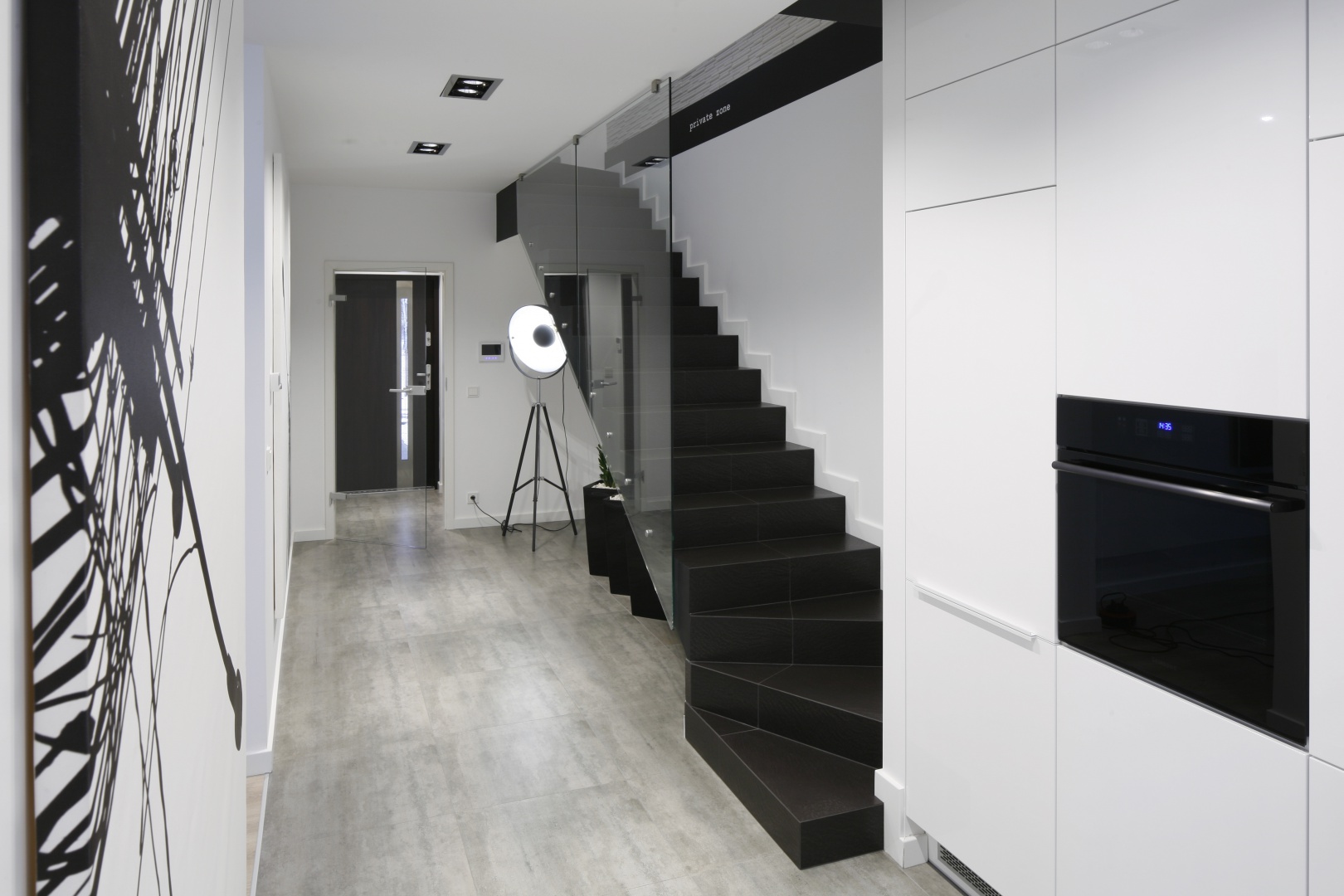 Eleganckie czarne stopnie, przesłonięte szklaną balustradą wychodzą bezpośrednio na kuchnię. Projekt: Karolina Stanek-Szadujko, Łukasz Szadujko. Fot. Bartosz Jarosz