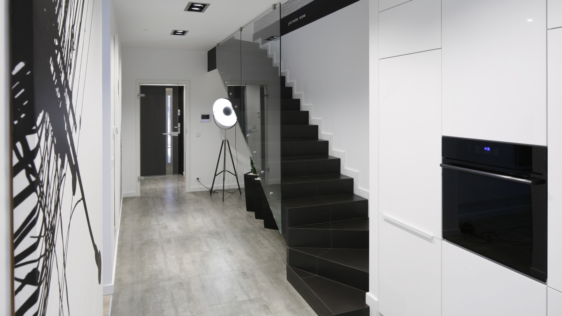Eleganckie czarne stopnie, przesłonięte szklaną balustradą wychodzą bezpośrednio na kuchnię. Projekt: Karolina Stanek-Szadujko, Łukasz Szadujko. Fot. Bartosz Jarosz