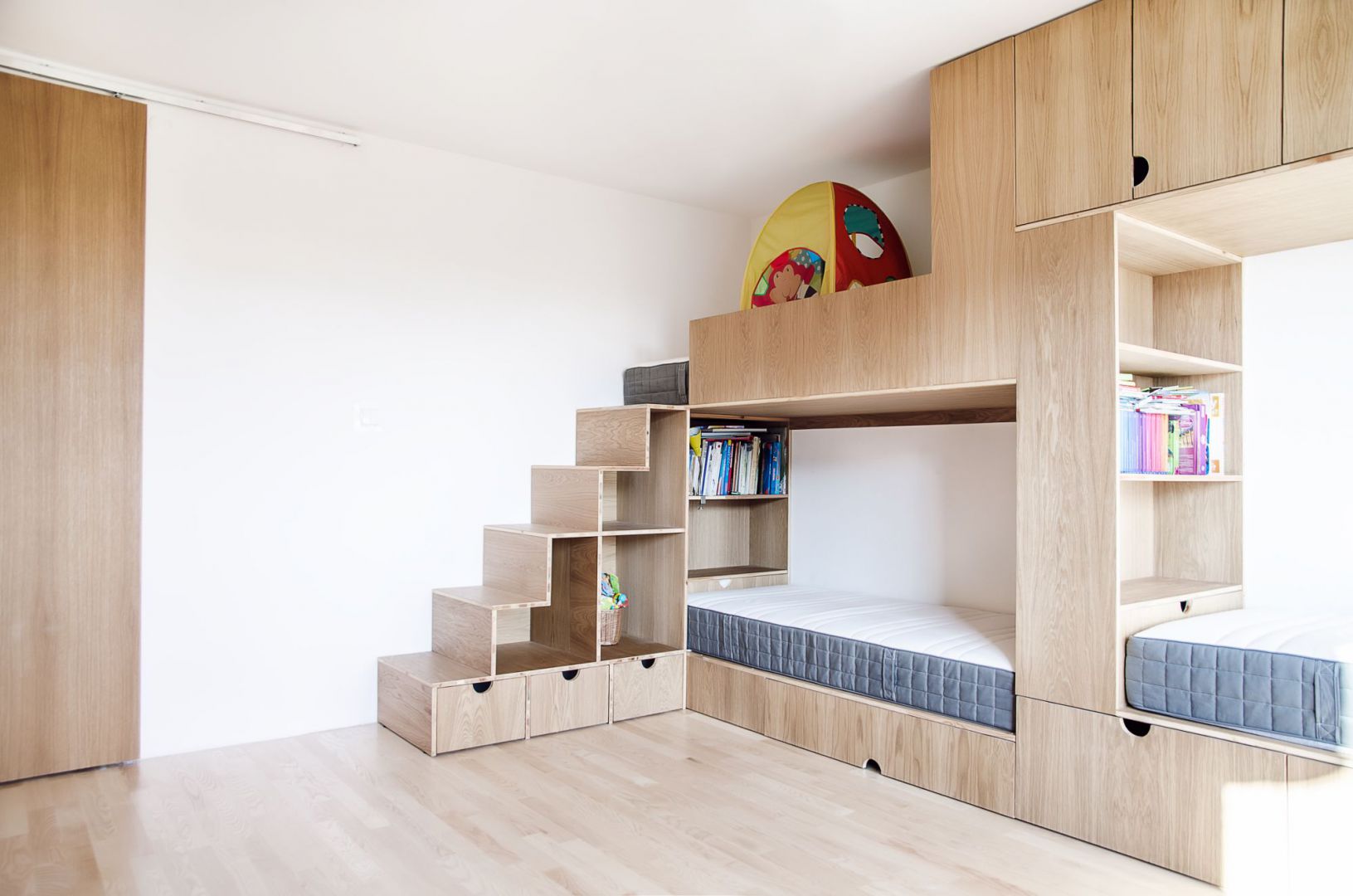 Żeby maksymalnie wykorzystać przestrzeń w pokoju dziewczynek, jedną ze ścian zabudowano trzyosobowym meblołóżkiem. Projekt: Atelier Starzak Strebicki. Fot. Mateusz Bieniaszczyk