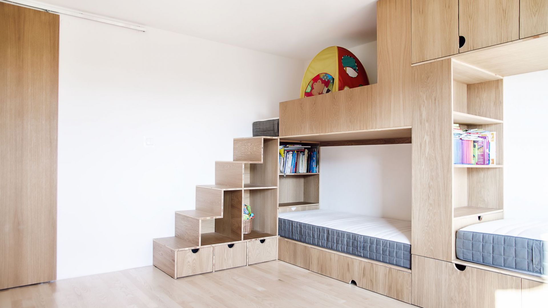 Żeby maksymalnie wykorzystać przestrzeń w pokoju dziewczynek, jedną ze ścian zabudowano trzyosobowym meblołóżkiem. Projekt: Atelier Starzak Strebicki. Fot. Mateusz Bieniaszczyk