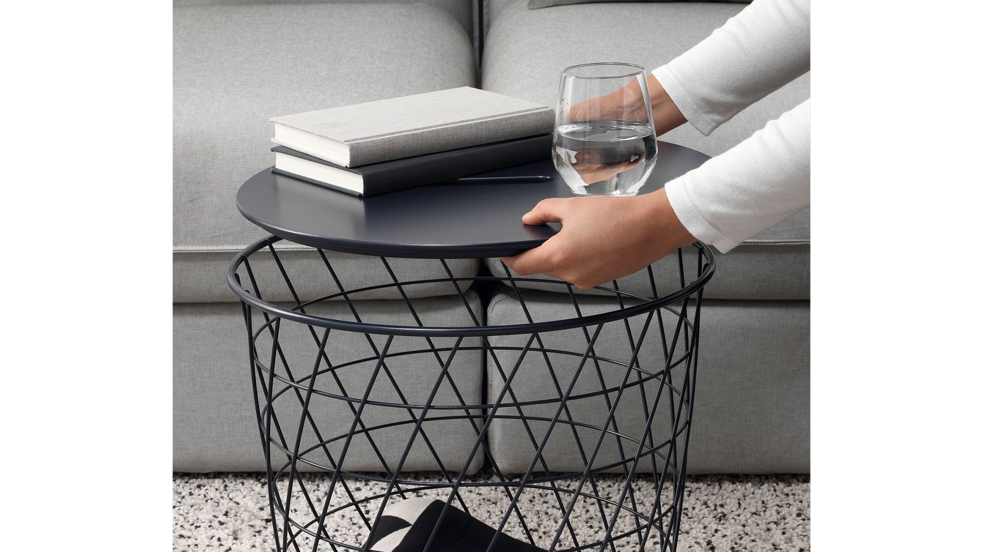 Stolik Kvistbro z miejscem do przechowywania, granatowy. Uchwyt umieszczony w blacie stołu ułatwia otwieranie i sięganie po przedmioty przechowywane w koszyku. Fot. IKEA