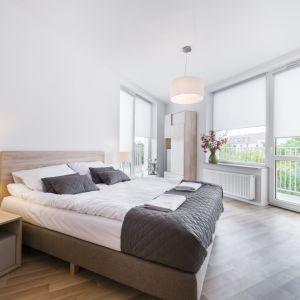 Sypialnia w stylu skandynawskim. Podobnie jak w innych pomieszczeniach znaleźć w niej można proste meble, duże okna, białe ściany i drewnianą podłogę. drewnianeFot. Shutterstock