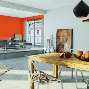 Eleganckie szarości w strefie kuchni i jadalni przełamano wyrazistym pomarańczem na jednej ze ścian w salonie. Fot. Magnat