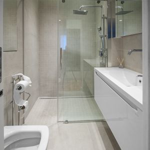 We wnętrzu łazienki jasnobeżowe płytki stanowią tło dla bieli zabudowy i szkła. Fot. Progetti Architektura