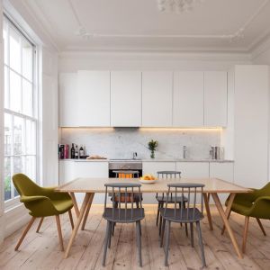 Centrum kuchni stanowi drewniany stół. Dużą zaletą tego wnętrza jest duże okno, przez które wpada naturalne światło, tworząc przyjazny klimat. Fot. Architecture for London 