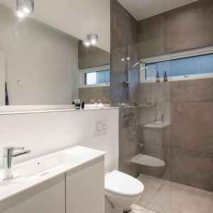 W łazience dominują szarości oraz biała nowoczesna armatura. Architekci zdecydowali się na prysznic z odpływem liniowym. Fot. Julian Weyer