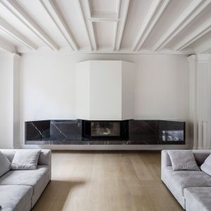 Białe, historyczne otwarte wnętrza ociepla drewniana podłoga oraz luksusowy kominek z kamienia. Fot. Adrià Goula Sardà