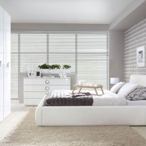 Sypialnia w bieli nie musi być monotonna. Ściana za łóżkiem wykończona dekoracyjną tapetą to świetny element wnętrza. Fot. BRW