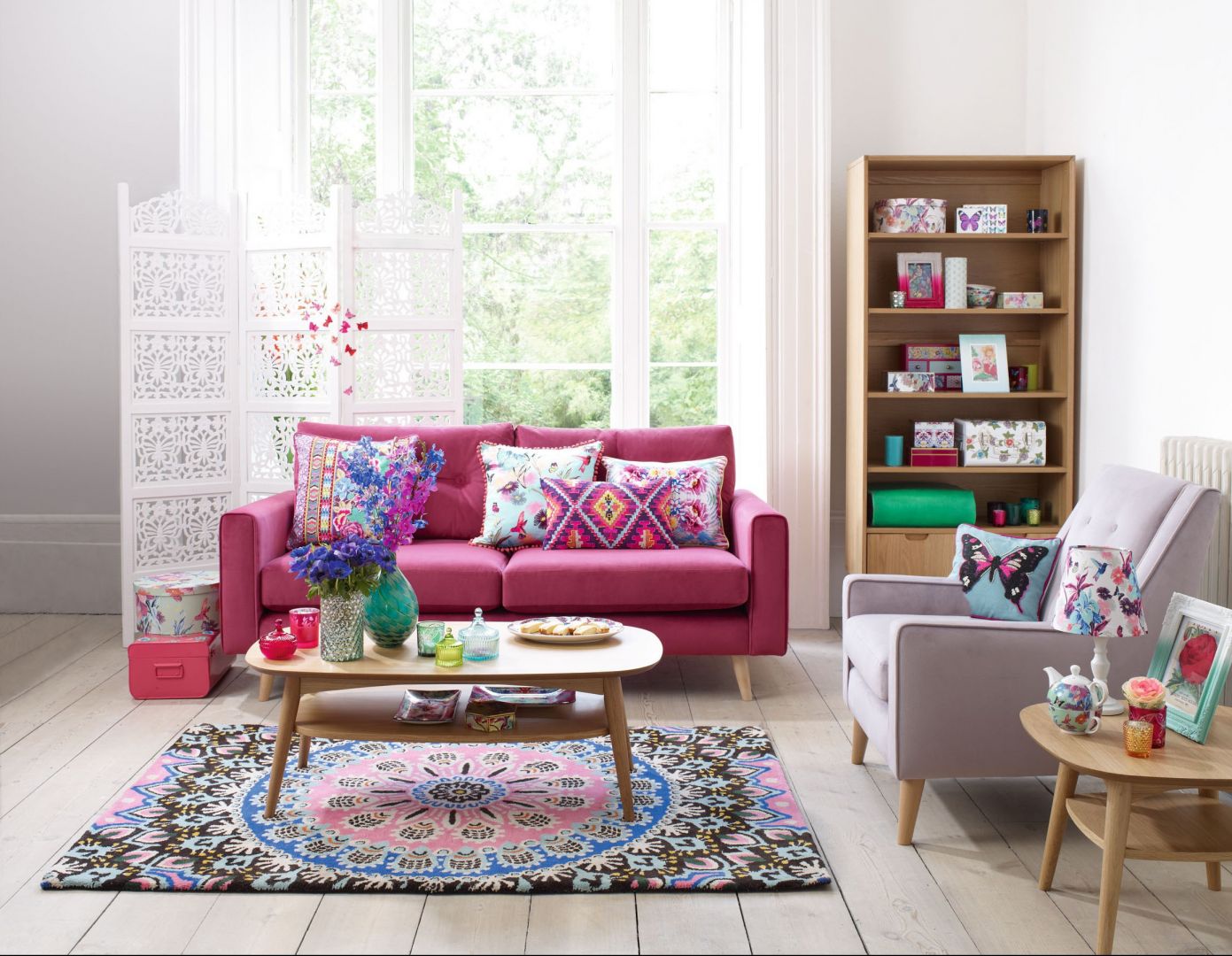 Duży pokój w mieszkaniu lubi zdecydowane barwy. Różowa sofa doskonale współgra z etnicznymi wzorami poduszek i dywanu. Fot. Debenhams