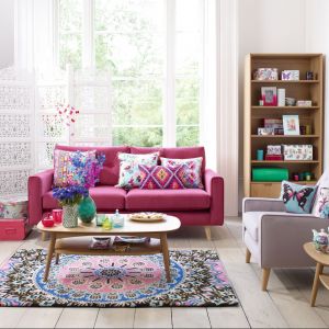Salon jest przestrzenią, która lubi zdecydowane barwy. Różowa sofa doskonale współgra z etnicznymi wzorami poduszek i dywanu. Fot. Debenhams