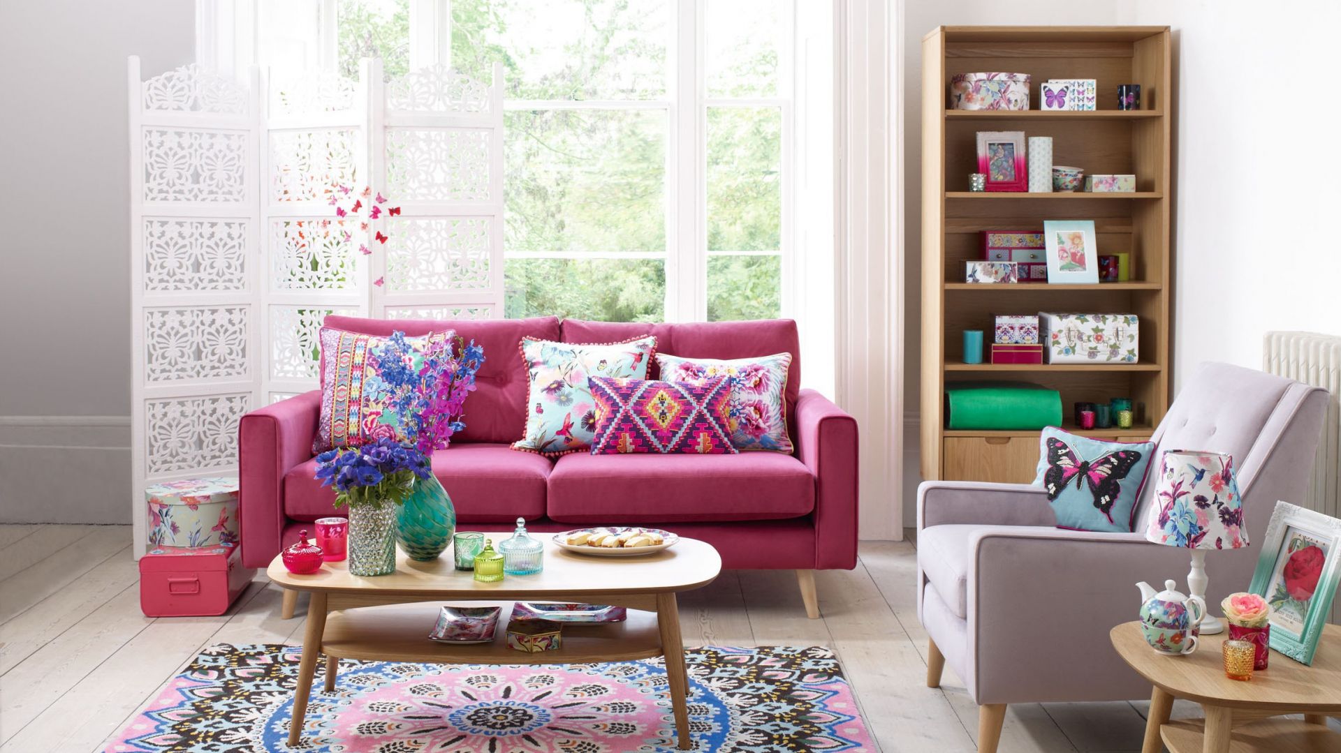 Duży pokój w mieszkaniu lubi zdecydowane barwy. Różowa sofa doskonale współgra z etnicznymi wzorami poduszek i dywanu. Fot. Debenhams