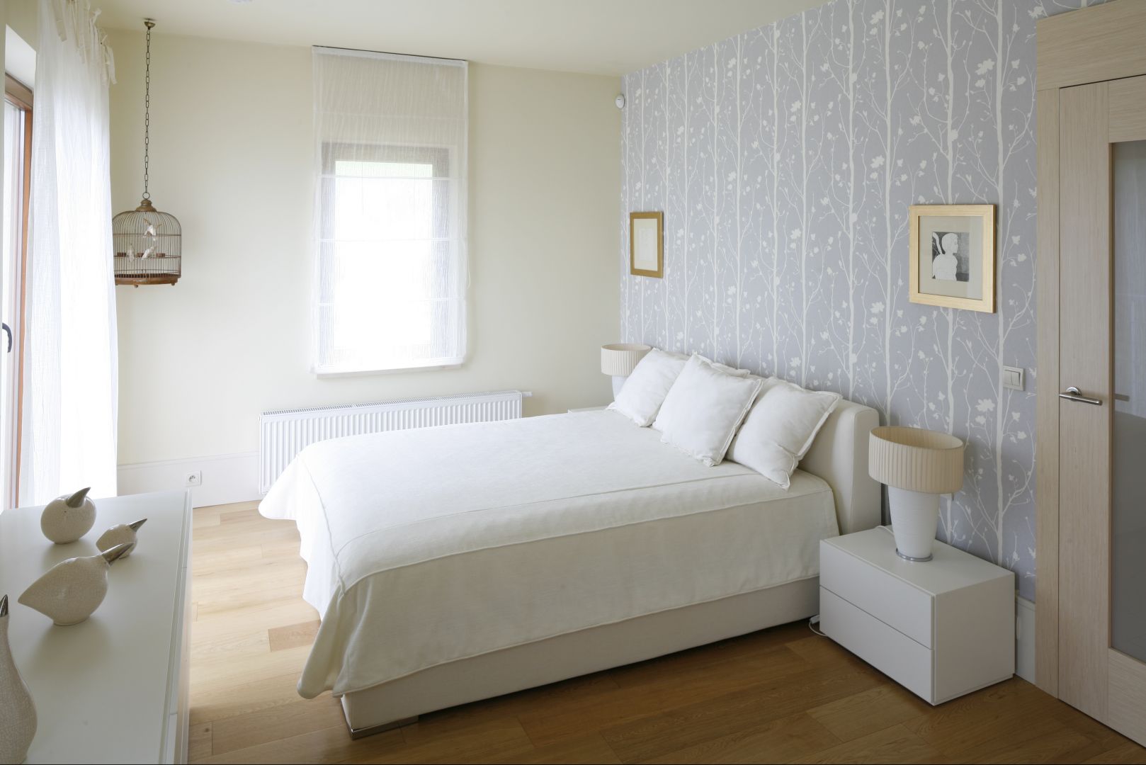 Białe łóżko usytuowane centralnie na największej ścianie w sypialni, która jednocześnie stanowi najbardziej widoczny element w pokoju, ponieważ została udekorowana tapetą. Projekt: Małgorzata Borzyszkowska. Fot.Bartosz Jarosz