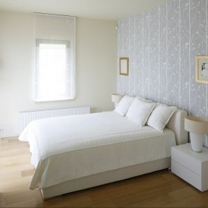 Białe łóżko ustawiono centralnie przy największej ścianie w sypialni. Stanowi ono widoczny element w pokoju, ponieważ została udekorowana tapetą. Projekt: Małgorzata Borzyszkowska. Fot. Bartosz Jarosz