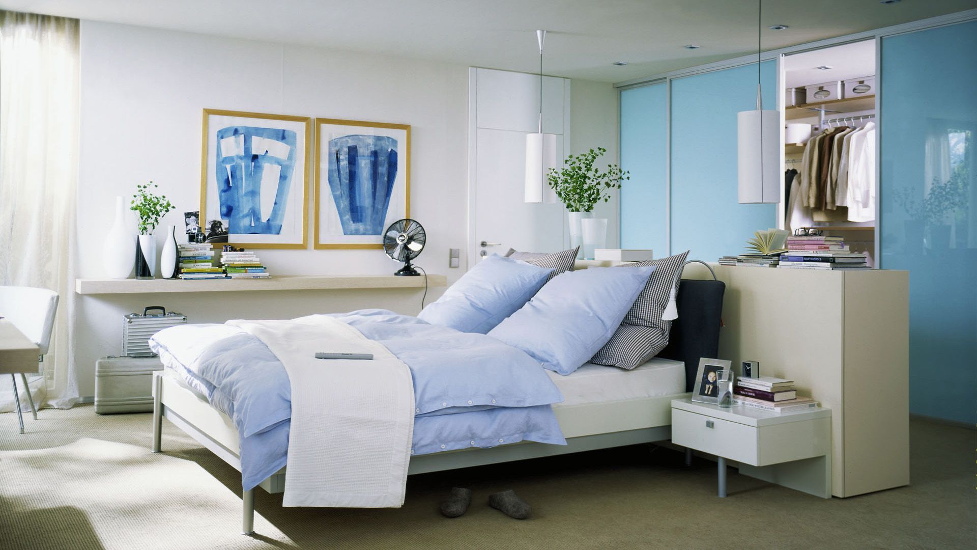 Duża sypialnia z ciekawie zagospodarowaną garderobą, która została usytuowana za wezgłowiem łóżka. Połączenie błękitu i bieli tworzy tu chłodną, ale przyjemną aranżację. Fot. Raumpuls