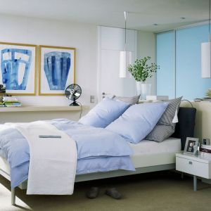 Duża sypialnia z ciekawie zagospodarowaną garderobą, która została usytuowana za wezgłowiem łóżka. Połączenie błękitu i bieli tworzy tu nowoczesną, ale przyjemną aranżację. Fot. Raumpuls