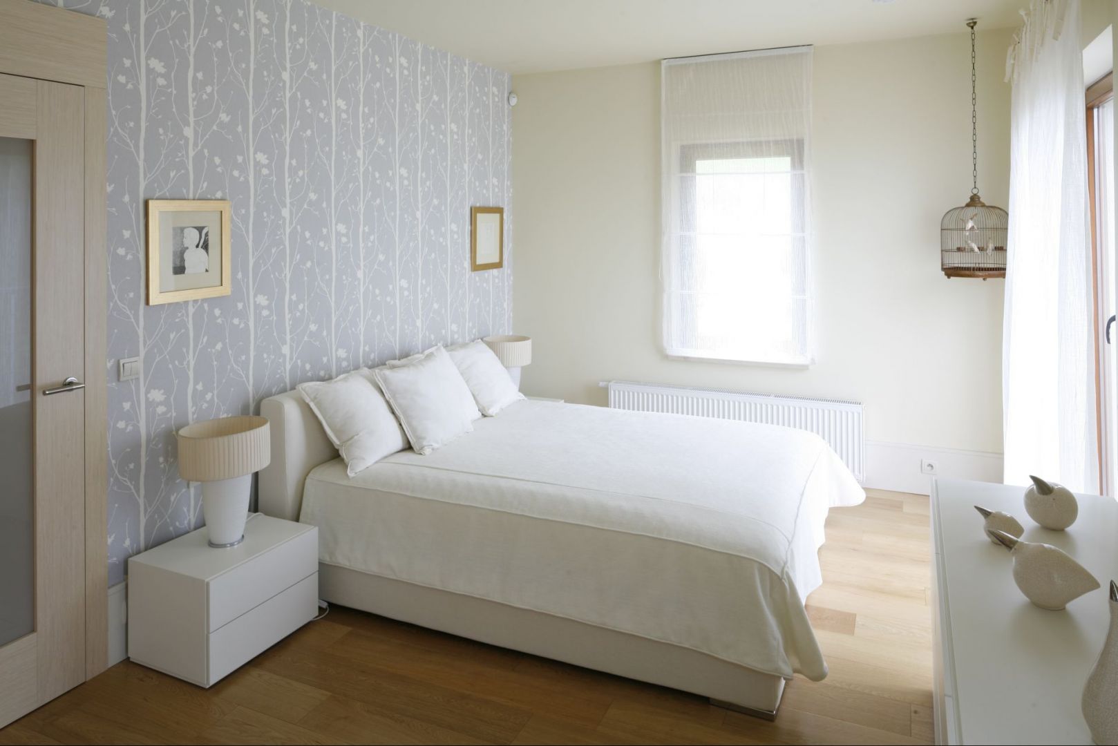 Białe łóżko usytuowane centralnie na największej ścianie w sypialni, która jednocześnie stanowi najbardziej widoczny element w pokoju, ponieważ została udekorowana tapetą. Proj. Małgorzata Borzyszkowska. Fot.Bartosz Jarosz