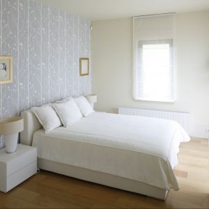 Białe łóżko zostało usytuowane centralnie na największej ścianie w sypialni, która jednocześnie stanowi najbardziej widoczny element w pokoju, dzięki dekoracyjnej tapecie. Projekt: Małgorzata Borzyszkowska. Fot. Bartosz Jarosz