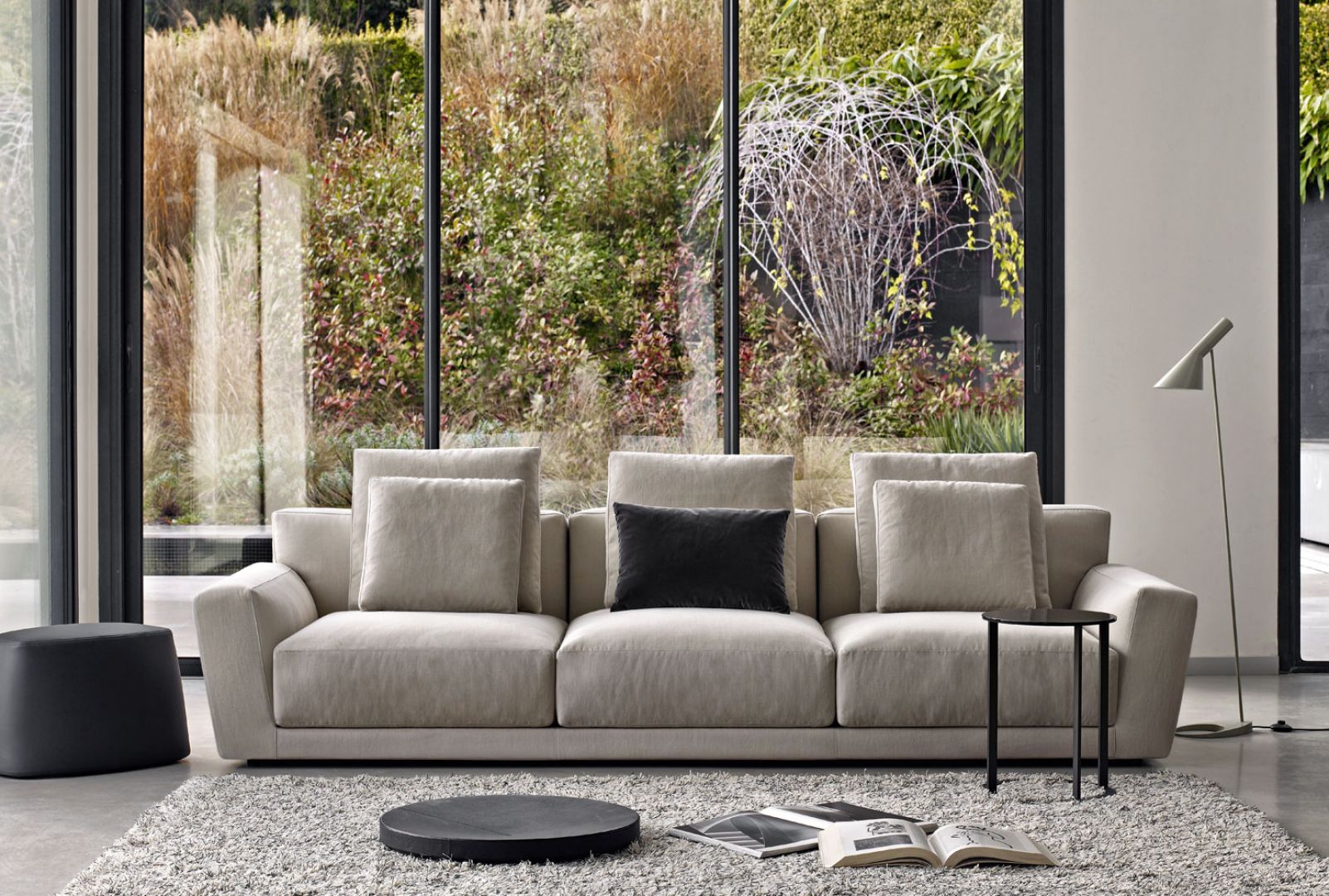 Sofa z dużymi, miękkimi poduchami na oparciu i ciepłym kolorze szarym, lekko wymieszany z beżem. Fot. B&B italia