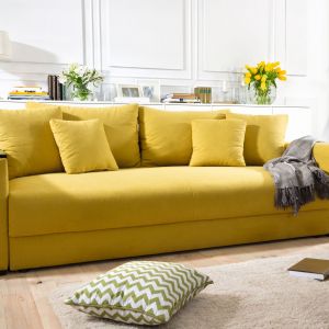 Sofa "Peter mega lux" ma przyjemną, żółtą barwę. Na jednym z podłokietników umieszczona jest drewniana półeczka, która można posłużyć za podręczny stoliczek na kubek z kawą. Fot. Black Red White